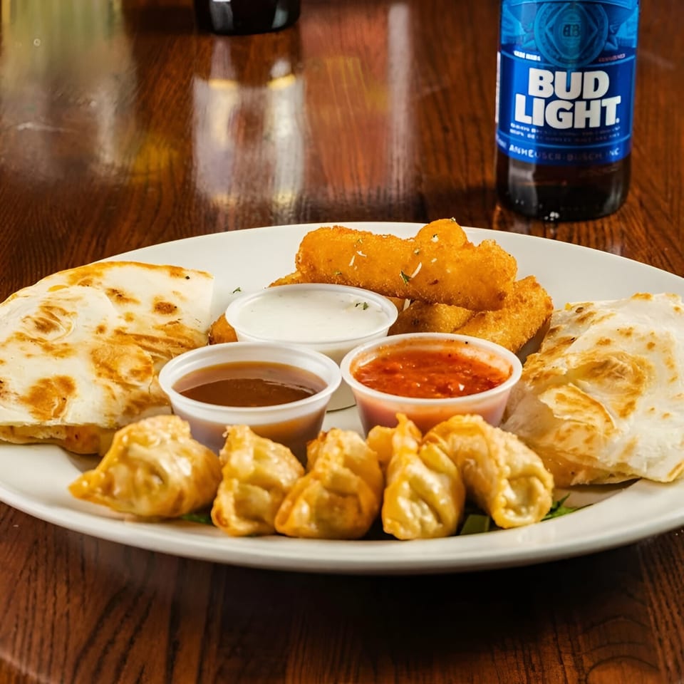 A platter of quesadillas, mozzarella sticks, and dumplings with dipping sauces and a Bud Light.