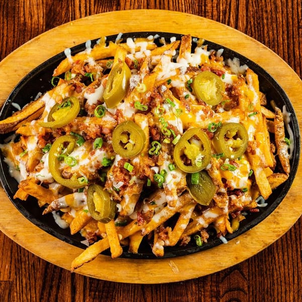 Loaded fries with melted cheese, bacon bits, jalapeños, and green onions in a cast iron skillet.