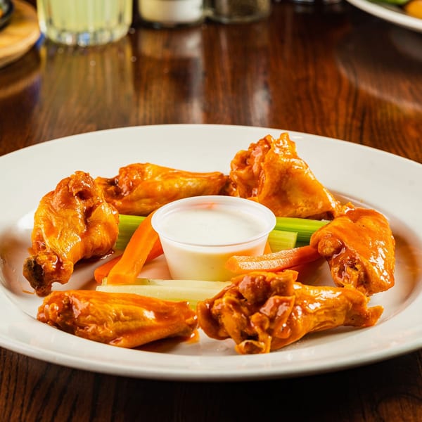 A plate of buffalo wings with ranch dressing, carrots, and celery on a wooden table.