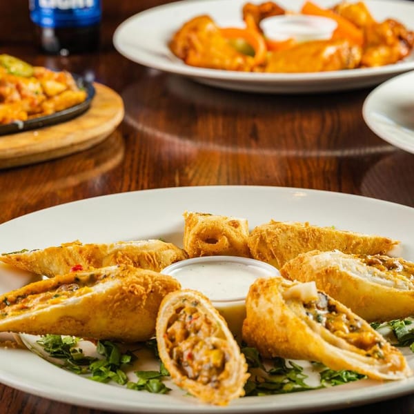 Crispy fried egg rolls with a creamy dipping sauce, served on a white plate at The Back 9 Addison.