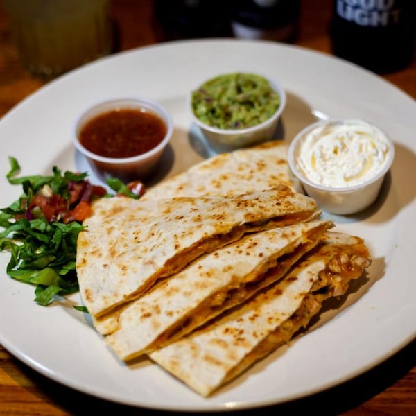 Quesadillas with sides of salsa, guacamole, sour cream, and a small salad on a white plate.