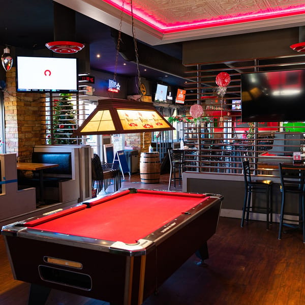 A red-felt pool table dominates the foreground of The Back 9 Addison sports bar, with booths and TVs.