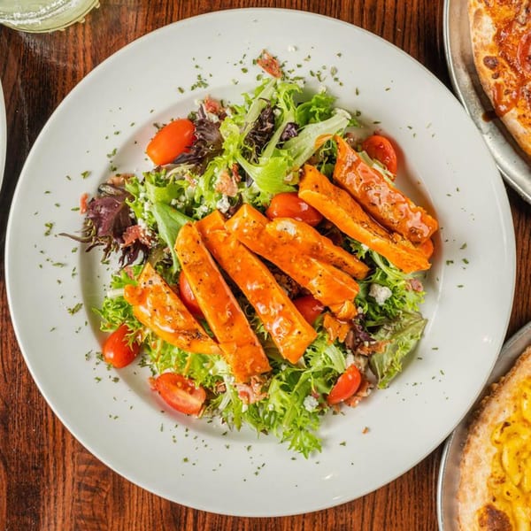 Overhead view of a fresh salad with buffalo chicken strips, cherry tomatoes, and crumbled cheese.