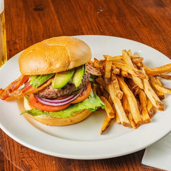 A bacon avocado burger with lettuce, tomato, and red onion, served with a side of fries.